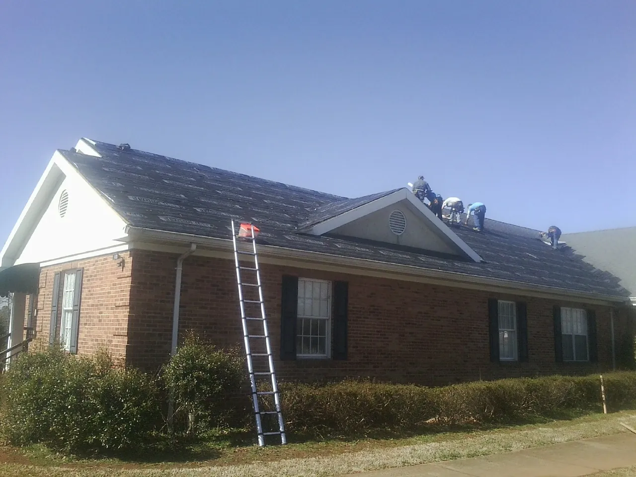 Crew tearing shingles off a brick ranch roof with a ladder set — Emergency Roof Repair work by our crew in Walnut Creek