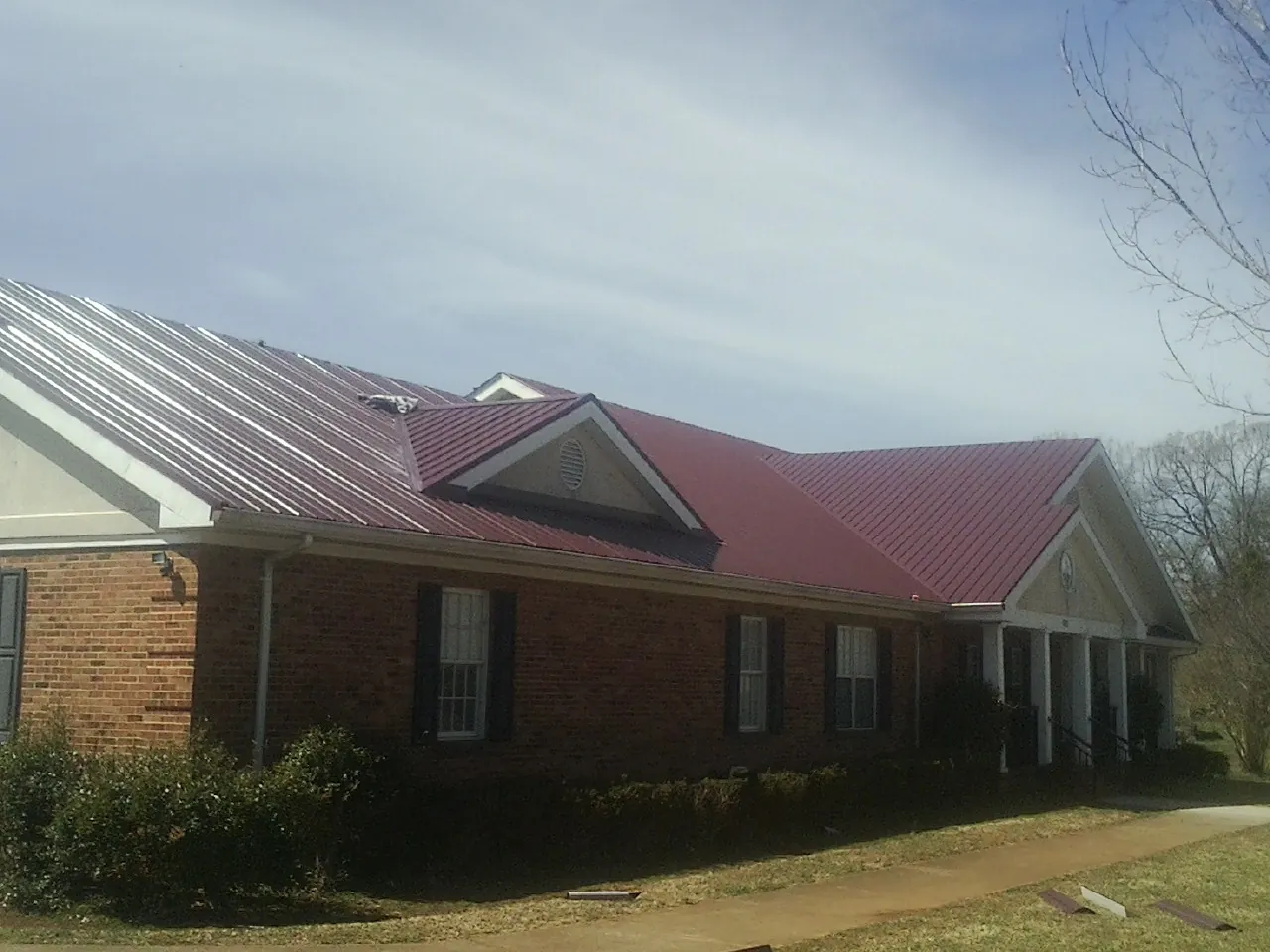 Red metal roof with gabled entries on a long brick building, from a Hail Damage Roof Repair job in Walnut Creek