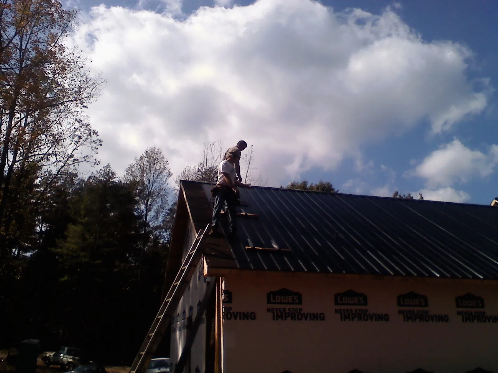 Roofer fastening dark metal panels high against a cloudy sky, from a Roof Inspection job in Walnut Creek