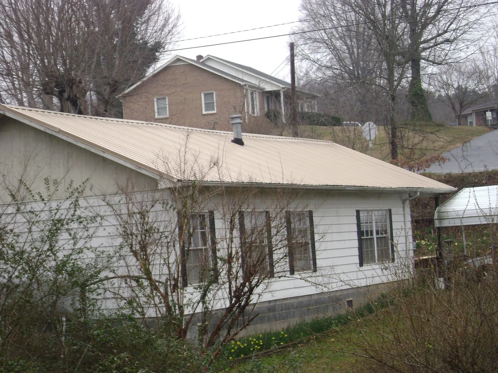 Tan metal roof on a white sided house set into a hillside — Commercial Roofing by Roofing Brothers in Walnut Creek